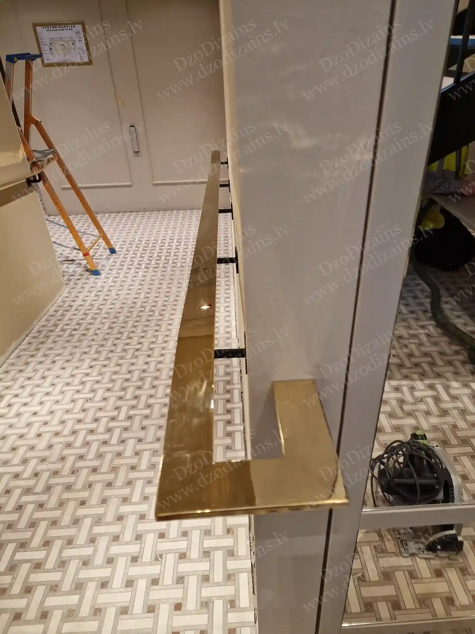 Крупный план полированного L-образного поручня под латунь золотого цвета на чёрной металлической и стеклянной системе ограждения во время ремонта интерьера