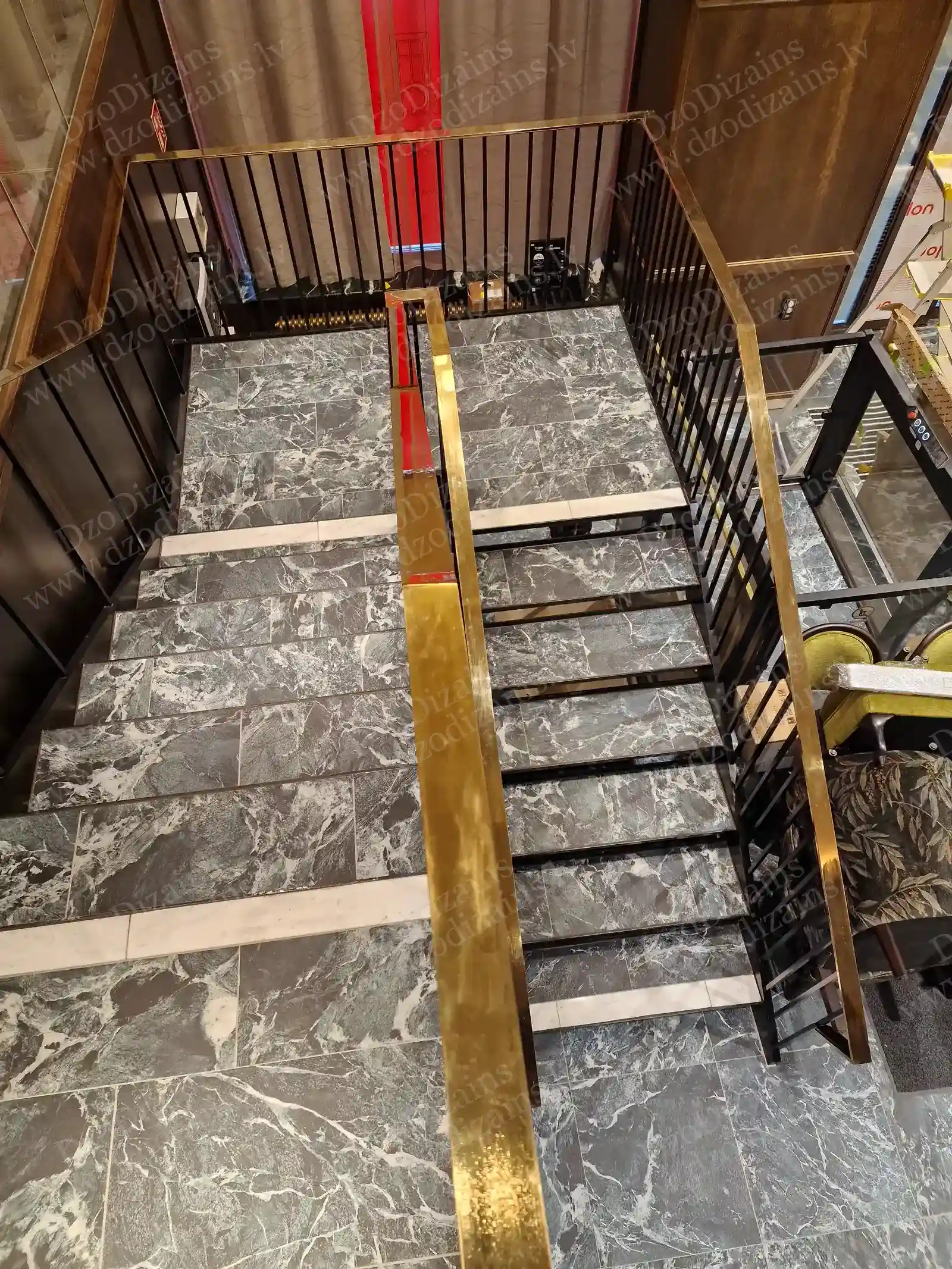 Вид сверху на современную лестницу из чёрного металла с серой мраморной плиткой и полированными поручнями под латунь золотого цвета в роскошном современном интерьере